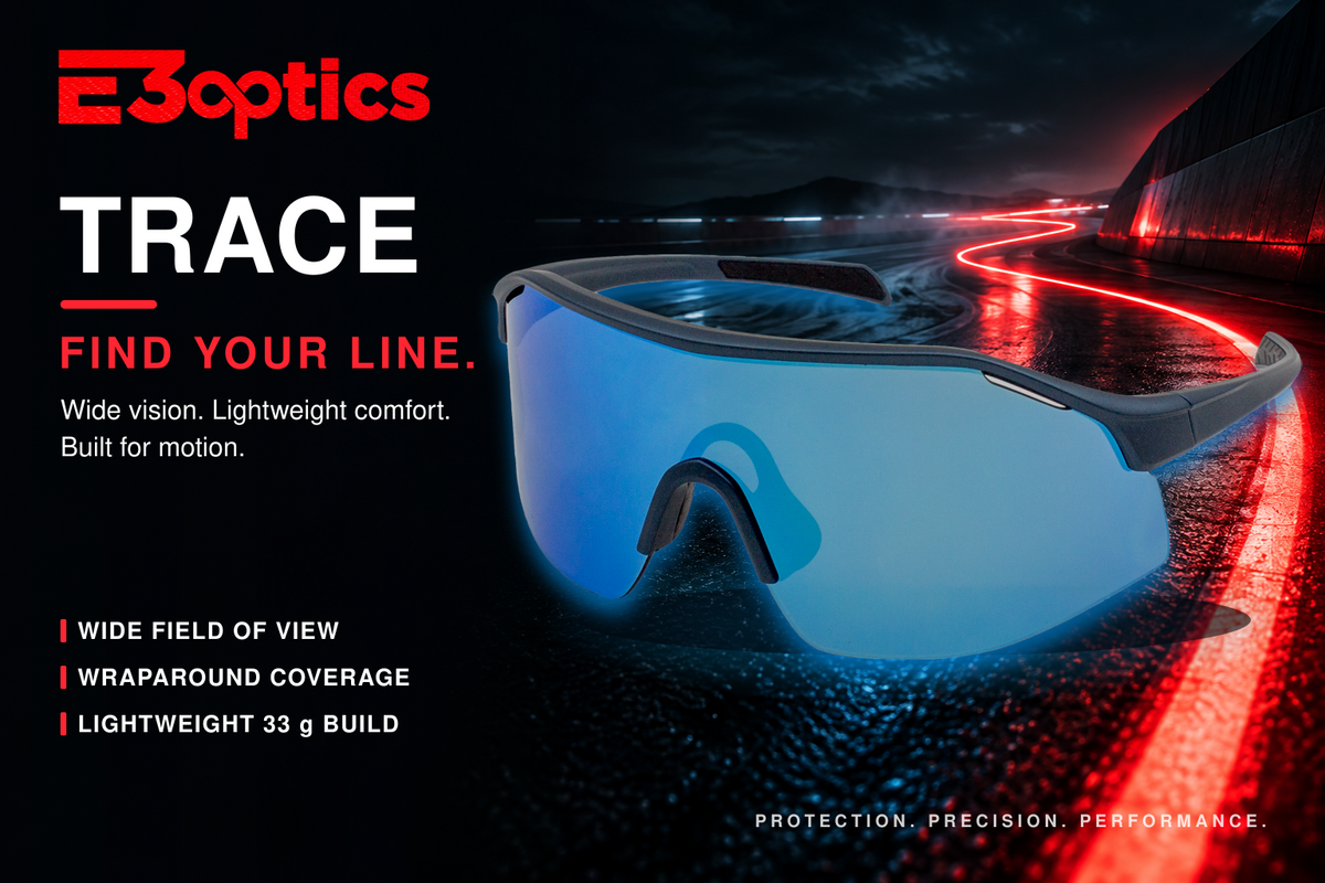 E3optics TRACE athletic shield sunglasses with a blue mirrored lens and gray frame, shown on a dark road with red light trails. Text highlights wide vision, lightweight comfort, and built for motion performance.