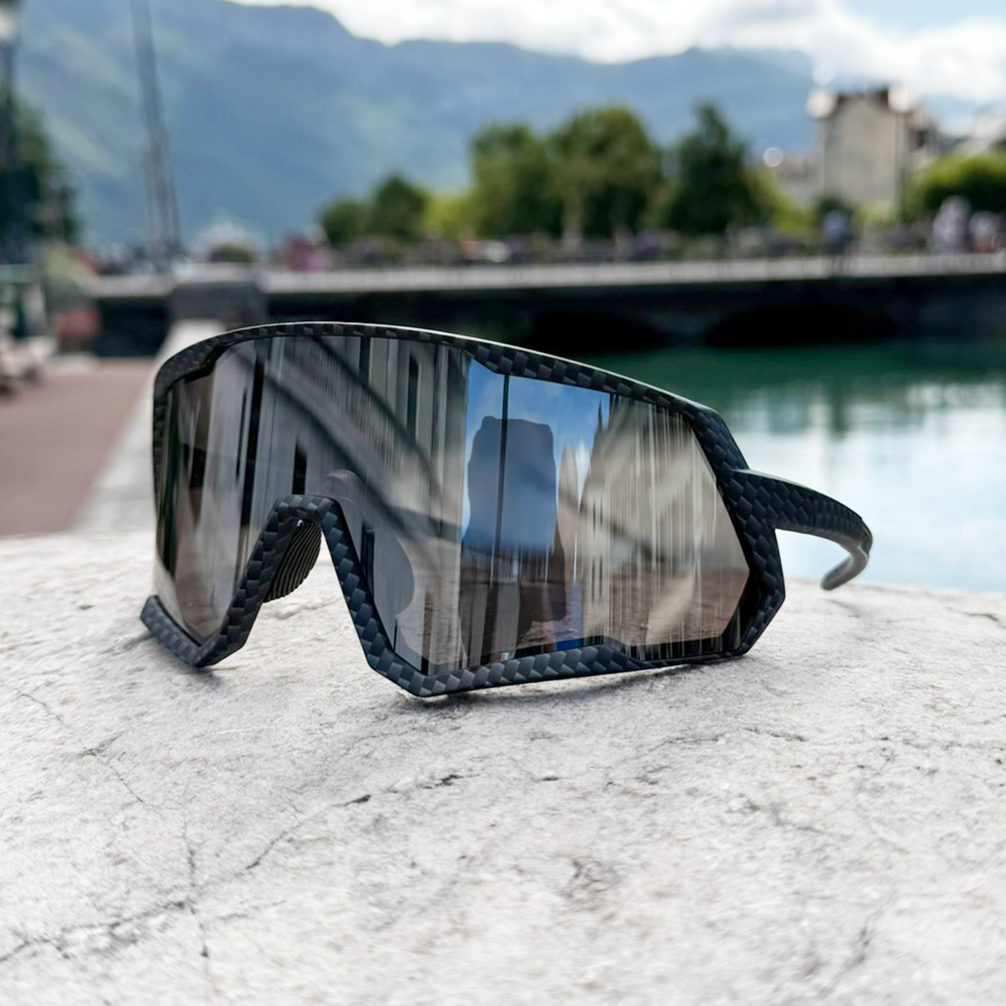 E3 Optics E6 sunglasses in carbon black precise lens displayed by a river with mountains in the background