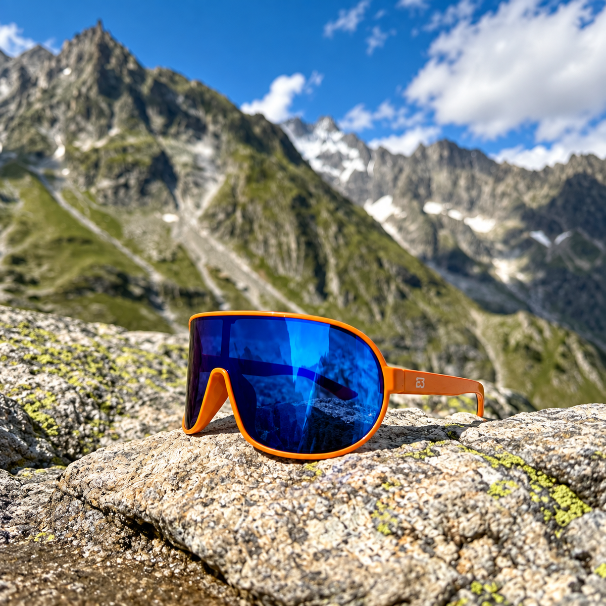 Orange wraparound sunglasses with blue mirrored lenses resting on a rocky mountain surface, with a blurred alpine landscape and blue sky in the background.