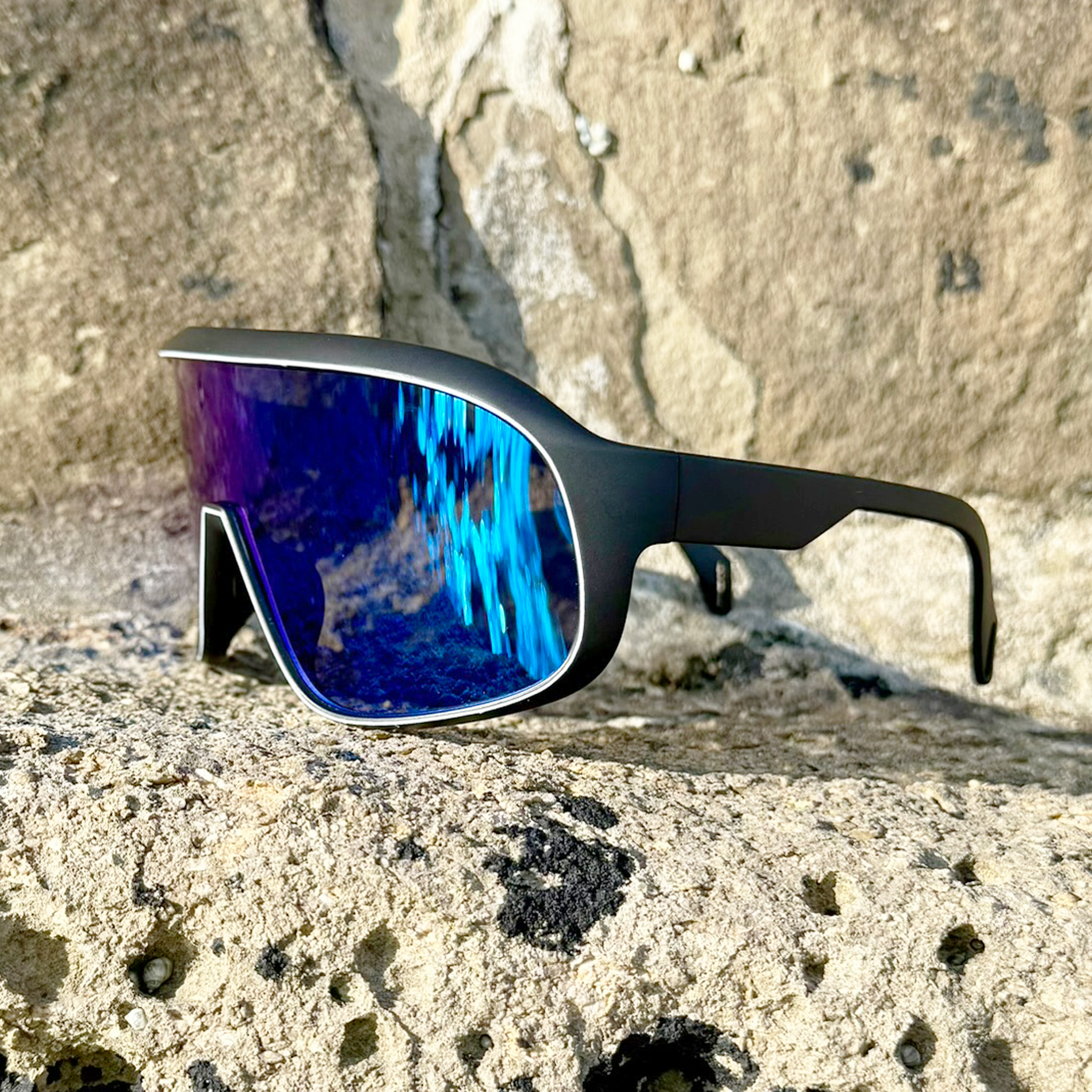 E3 Optics E10 polarized sunglasses on cliffside rock with reflective blue mirrored lenses.