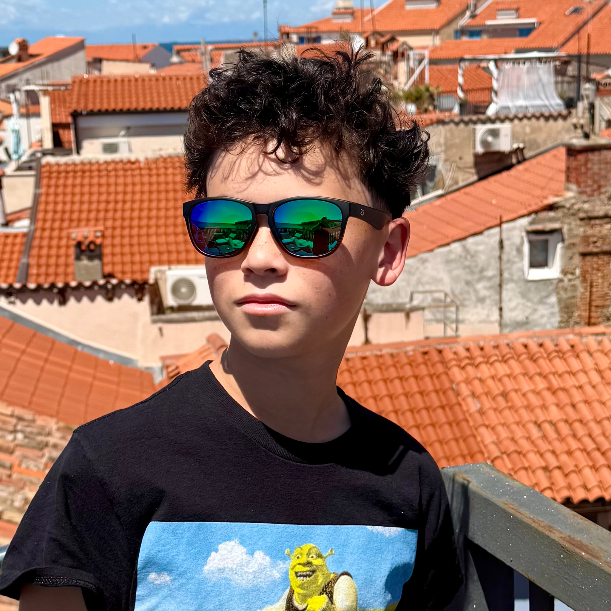 Person wearing sunglasses with a cityscape of buildings with red roofs in the background