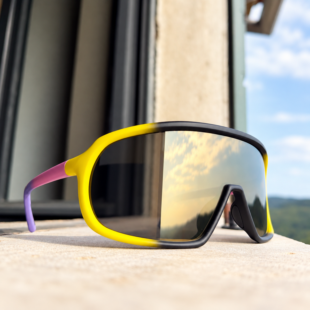 Sport sunglasses with a bright yellow and black frame, purple temple tips, and a mirrored lens reflecting a sunset sky, resting on a stone ledge outdoors.