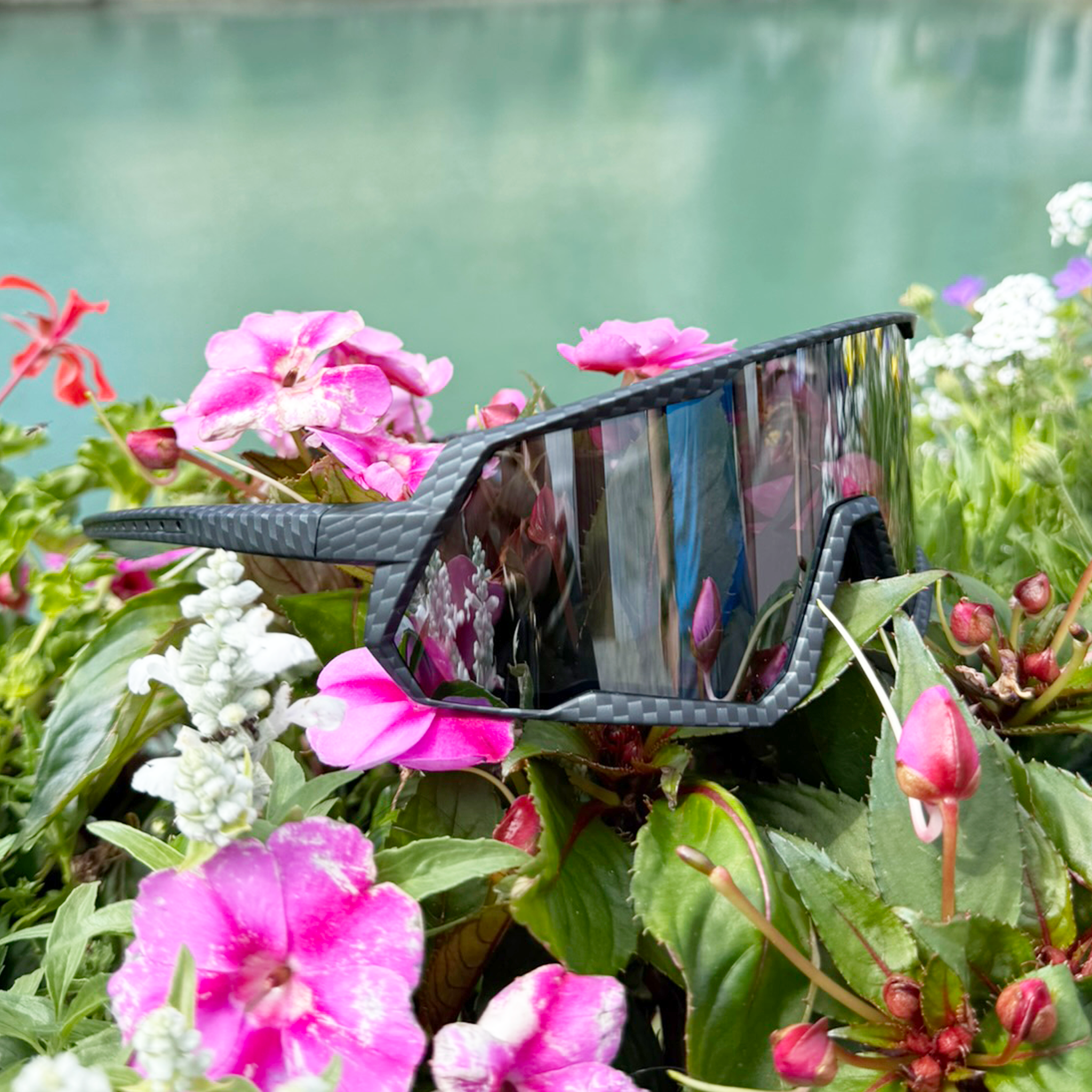 E3 Optics E6 sunglasses in carbon black precise lens resting among flowers by a riverside
